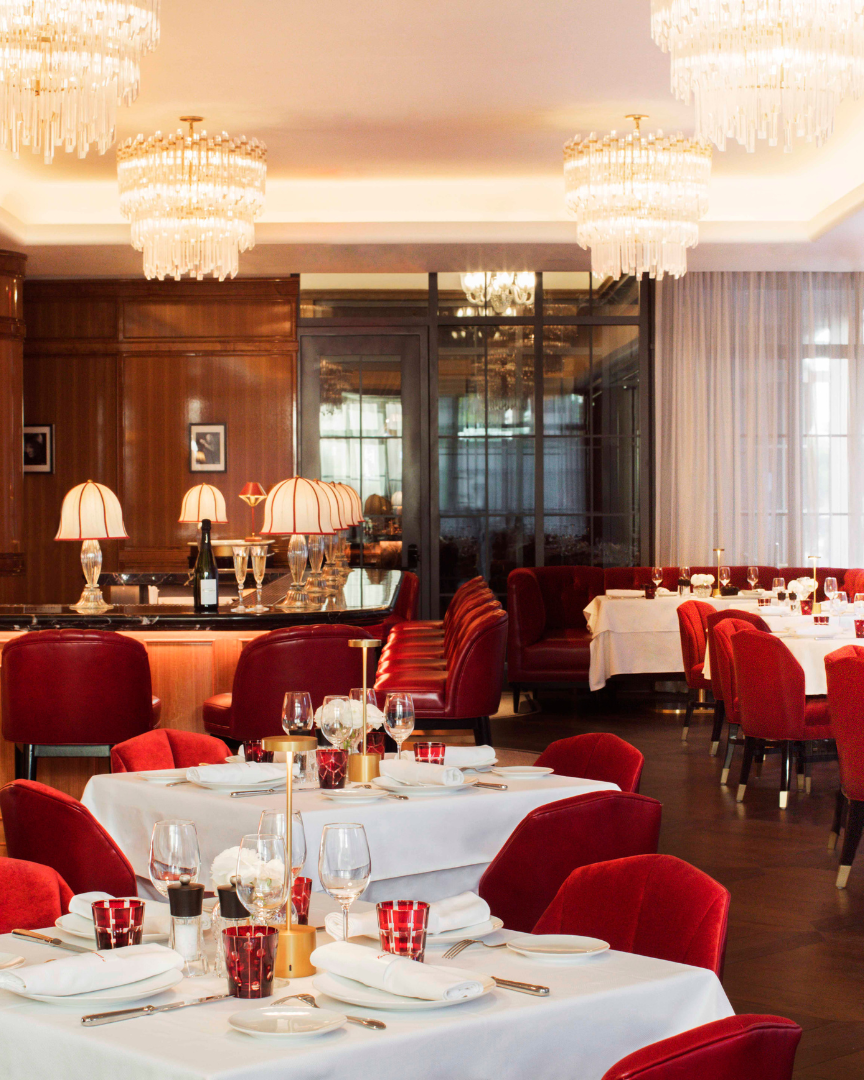 Luxurious restaurant interior with red chairs, white tablecloths, and chandeliers.