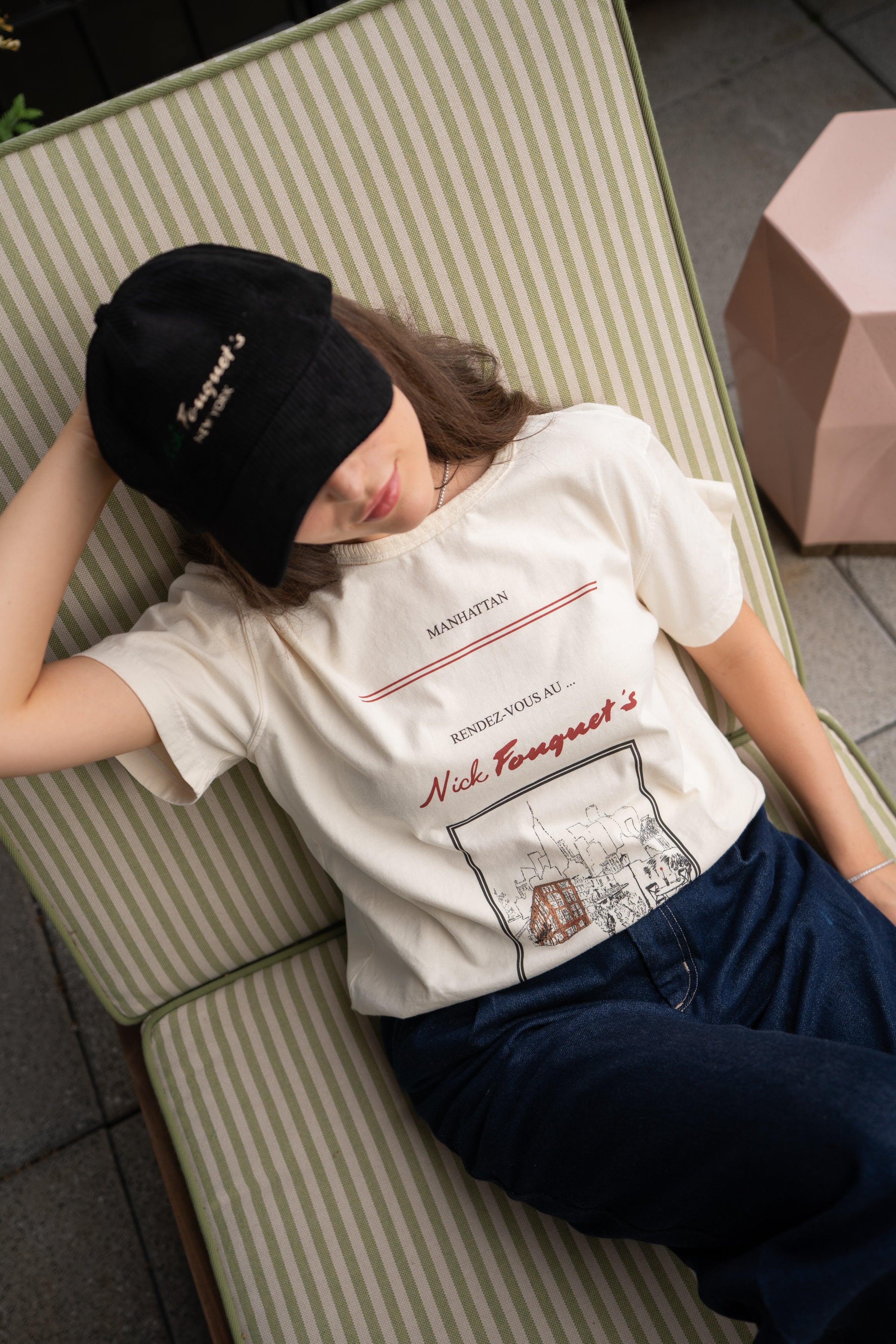 Person wearing a white t-shirt with text and graphics, lying on a striped bench.